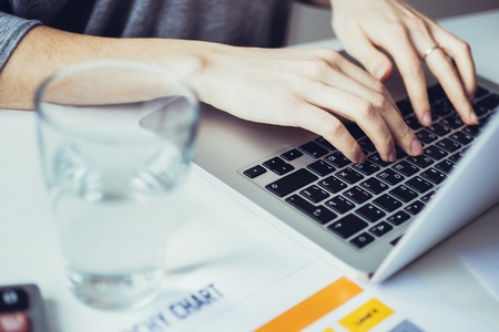 Close-up of female hands typing on laptop at table. Young businesswoman sitting at desk and workingの写真素材