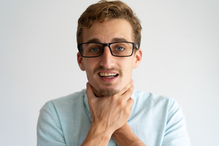 Closeup of stressed blonde guy imitating choke. Bored young Caucasian man in glasses keeping hands on his neck. Gesturing suicide conceptの写真素材