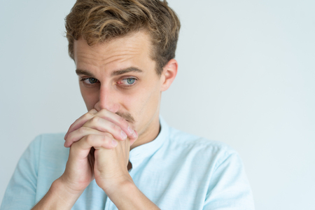 Thoughtful young man touching mouth with clenched hands and looking away. Handsome guy thinking....