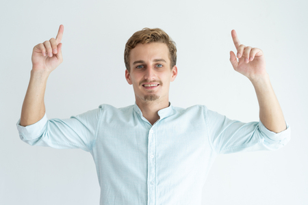 Smiling young man pointing forefingers upwards. Handsome guy recommending something. Promotion concept. Isolated front view on white background.の写真素材