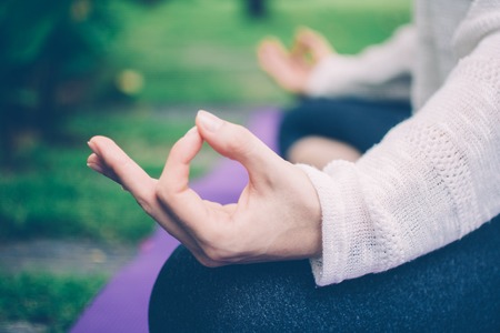 Close-up of female hand gesturing zen. Young woman wearing sweater sitting on mat and meditating outdoorsの写真素材