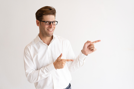 Cheerful handsome young man pointing both forefingers aside. Guy recommending something. Promotion concept. Isolated front view on white background.の写真素材