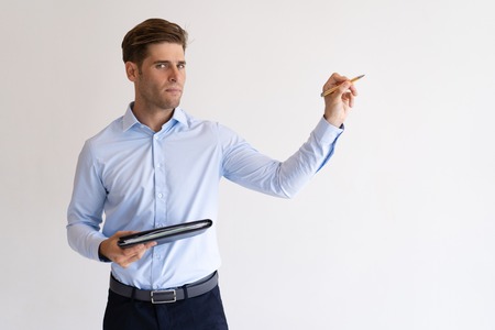 Serious young guy holding file and writing in air. Handsome business man giving lecture. Presentation concept. Isolated front view on white background.の写真素材