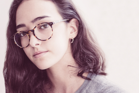Diligent female student wearing eyeglasses and looking at camera. Calm young lady with curly hair....