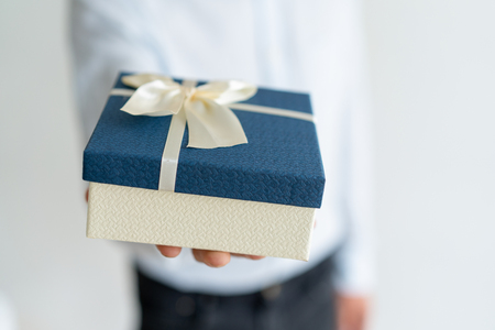 Closeup of gift on male hand. Unrecognizable man holding blue and white present box with ribbon and bow. Special day and festive event conceptの写真素材