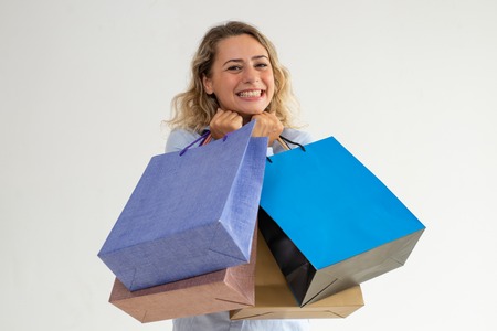 Cheerful positive curly-haired lady adoring shopping. Happy ecstatic woman holding heap of paper bags and looking at camera. Leisure conceptの写真素材