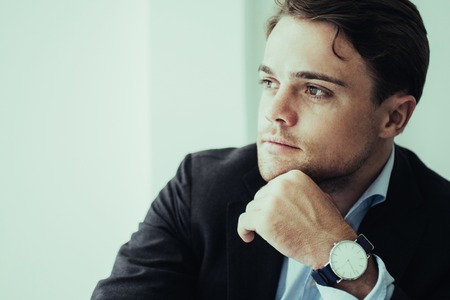Thoughtful young entrepreneur reflecting about own business. Pensive businessman touching chin and...