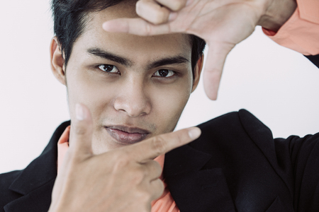 Close-up of face of confident young Asian businessman showing finger frame and looking at cameraの写真素材