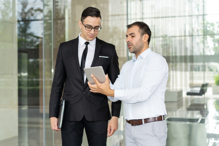 Confident businessman showing information on tablet computer to coworker. Business executives discussing new product presentation on digital tablet. Work discussion conceptの写真素材