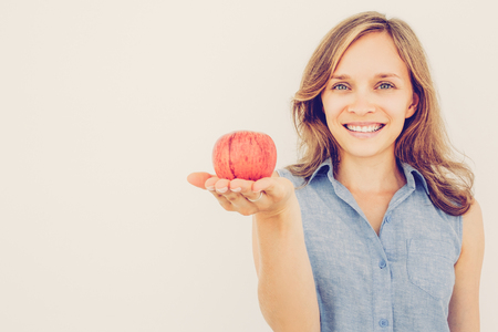 Closeup portrait of smiling young pretty woman looking at camera and holding red apple on palm. Isolated front view on grey background.の写真素材