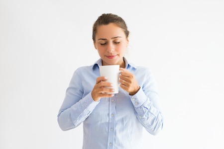 Smiling young woman holding mug, smelling and drinking tea. Pretty lady enjoying drinking tea or coffee with her eyes closed. Break concept. Isolated front view on white background.の写真素材