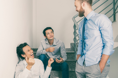 Closeup of three smiling middle-aged business men chatting, gesturing, standing and sitting on stairsの写真素材