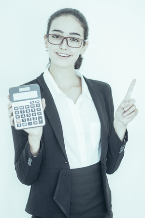 Portrait of cheerful young Caucasian female accountant wearing costume and glasses showing calculator, looking at camera and smilingの写真素材