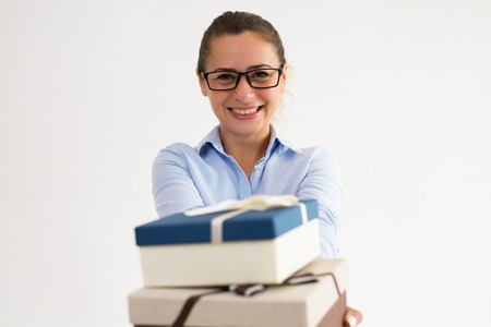 Positive office assistant preparing presents for corporate party. Smiling Caucasian woman in formal shirt giving gift boxes at camera. Corporate party or presenting conceptの写真素材