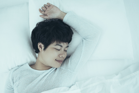 Closeup portrait of content young pretty Asian woman sleeping in bed in bedroom. Top view.の写真素材