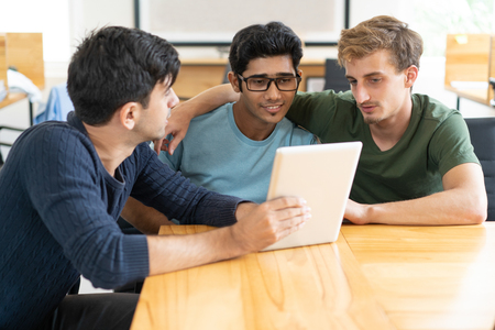 Hispanic man showing project idea on tablet to student friends. Pensive young men brainstorming about information together. Planning university project conceptの写真素材