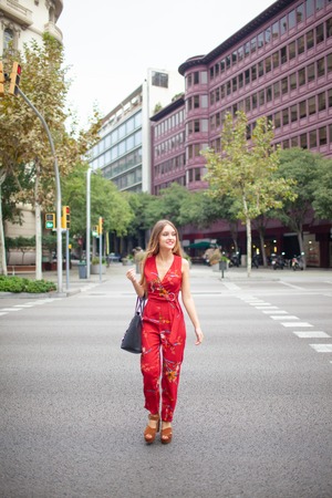 Happy city girl holding bag and crossing road outdoors. Positive attractive young woman in stylish jumpsuit walking in city. Tourist conceptの写真素材