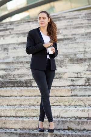 Pensive female manager walking around office building during lunch break and drinking takeaway coffee.の写真素材