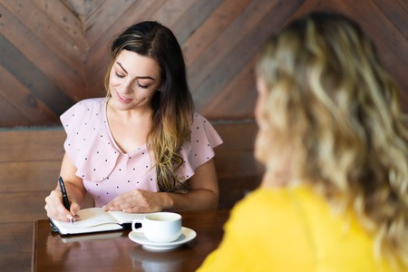 Two women drinking coffee and making notes in cafe.