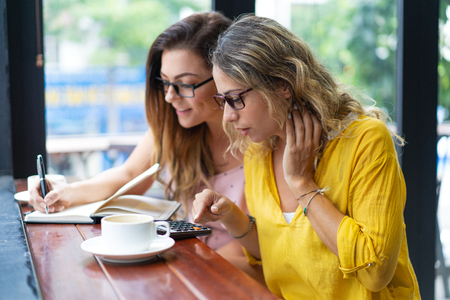 Serious women drinking coffee and working in cafe.の写真素材