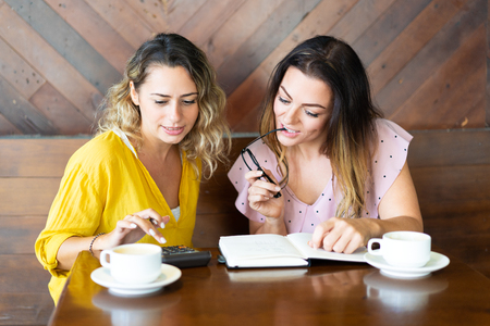 Pensive women drinking coffee and using calculator in cafe.の写真素材