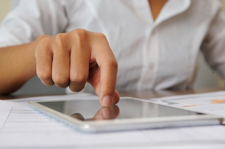 Closeup of person tapping on touchscreen. Tablet and papers lying on desk. Technology and paperwork concept. Cropped view.の写真素材