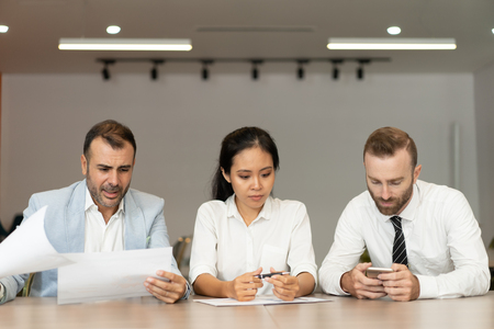 Focused business people working with documents at desk in office. Businesspeople sitting with...