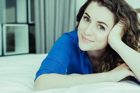 Closeup portrait of smiling young beautiful woman looking at camera and lying on bed in bedroom. Front view.の写真素材