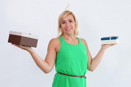 Positive woman holding two gift boxes on palms. Lady wearing party hat and looking camera. Party and...