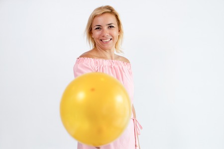 Smiling pretty woman giving balloon to viewer. Positive lady wearing summer dress and looking at...