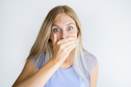 Portrait of shocked young woman covering mouth with hand. Caucasian blond girl standing shocked of news. Secrecy conceptの写真素材