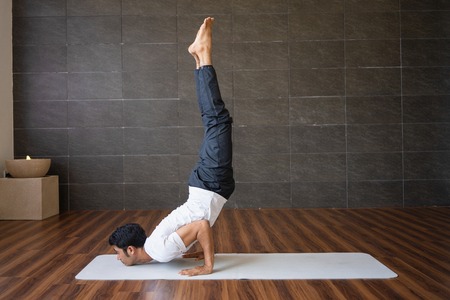 Experienced yogi doing handstand yoga pose in gym. Indian man practicing experienced yoga. Yogi concept. Side view.の写真素材
