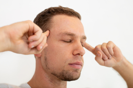 Thoughtful concentrated man touching temples with forefingers. Serious handsome guy with stubble keeping eyes closed. Focusing on thoughts conceptの写真素材