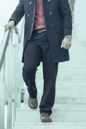 Stylish young Caucasian businessman wearing coat going downstairs outdoors. Business and fashion conceptの写真素材