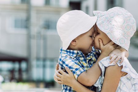 Closeup portrait of little boy and girl embracing and kissing outdoors. Side view.の写真素材