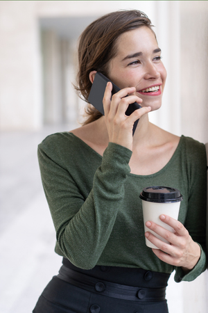 Portrait of happy young woman with coffee talking on phone. Caucasian businesswoman or student calling friend. Mobile communication conceptの写真素材