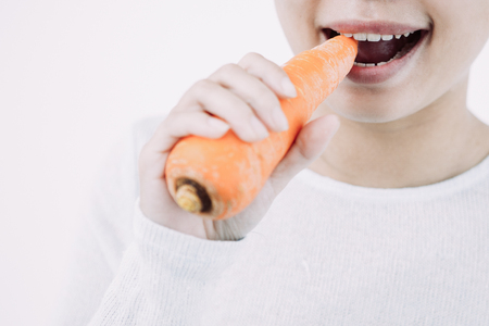 Young Asian woman eating fresh organic food. Close-up of girl biting carrot. Healthy lifestyle conceptの写真素材