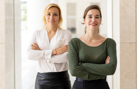 Successful team of two young business professionals. Confident positive businesswomen posing with arms crossed. Teamwork conceptの写真素材