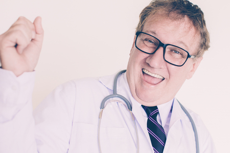 Closeup portrait of cheerful middle-aged male doctor looking at camera, celebrating success and pumping fist. Isolated view on white background.の写真素材