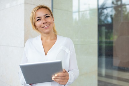 Portrait of happy young businesswoman working on pc tablet. Caucasian female manager standing at...