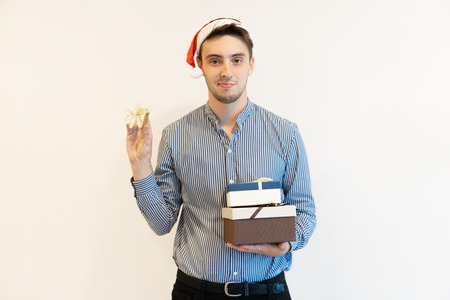 Content Christmas guy preparing gifts for friends and family. Sly young man holding gift boxes and...