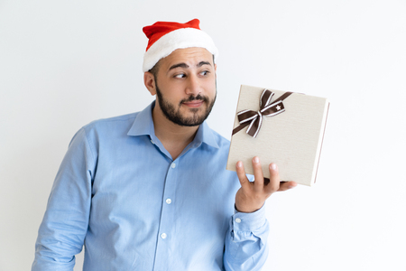 Curious man wearing Santa Claus hat and looking at gift box. Guy holding gift box. Christmas gift concept. Isolated front view on white background.の写真素材