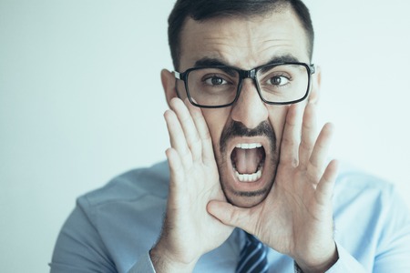 Closeup portrait of excited office worker in glasses opening mouth and shouting loud. Manager announcing important news. Announcement and warning conceptの写真素材