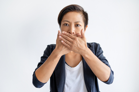 Shocked Asian woman covering mouth with both hands. Young lady looking at camera. Shock concept. Isolated front view on white background.の写真素材