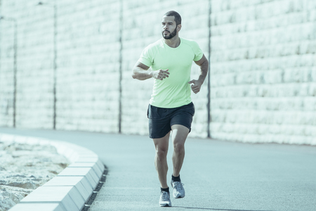 Pensive muscular young Caucasian man running along road. Handsome guy keeping fit and jogging. Sport and fitness conceptの写真素材