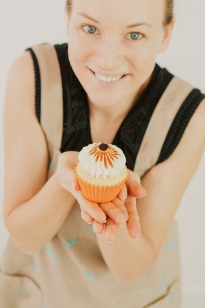 Closeup of smiling young Caucasian woman holding cupcake on palm. Food blogger preparing dessert for taking picture. Cooking and advertising conceptの写真素材