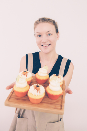 Closeup of smiling young Caucasian woman holding chopping desk with cupcakes. Mother preparing treat for children party. Cooking and festive conceptの写真素材