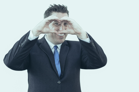 Cheerful handsome businessman making heart with fingers and looking through it at camera. Positive confident male lawyer doing his job with love. Taking care of business conceptの写真素材