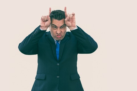Furious expressive businessman showing horns and looking at camera. Angry stubborn handsome salesman...