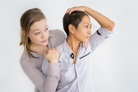 Serious women embracing and looking away. Multiethnic lesbian couple. Homosexual couple concept. Isolated front view on white background.の写真素材